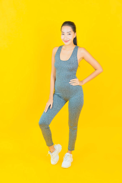 Retrato hermosa joven asiática mujer con ropa deportiva listo para el ejercicio sobre fondo amarillo - Foto, imagen