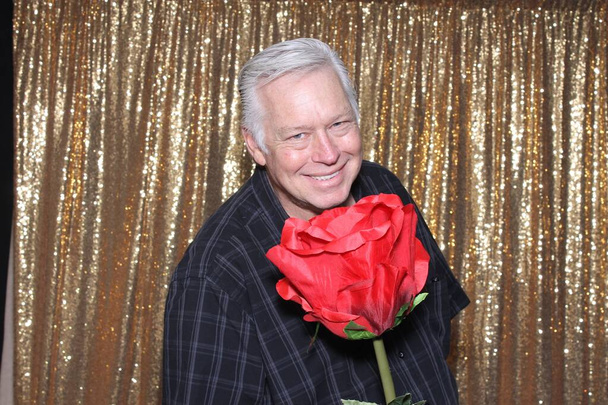 A happy middle aged man in a Photo Booth. A happy man laughs holds a Giant Red Rose as he smiles while in a Photo booth at a Party. Party Time Photo Booth. - Foto, Bild