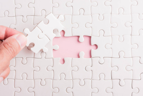 Top view flat lay of hand-holding last piece white paper jigsaw puzzle game last pieces put to place for solve problem complete mission, studio shot on a pink background, quiz calculation concept - Foto, afbeelding