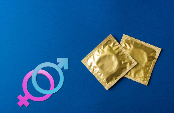 World sexual health or Aids day, Top view flat lay condom in wrapper pack and Male, female gender signs, studio shot isolated on a dark blue background, Safe sex and reproductive health concept - Photo, image