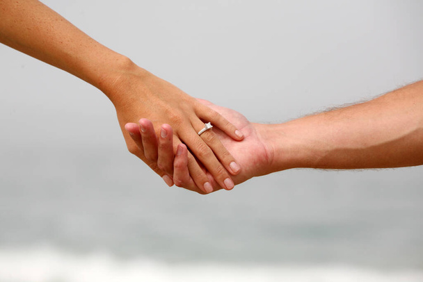 Помолвка Пара держась за руки с пляжным фоном. Пара взялась за руки с обручальным кольцом и фоном в Лагуна Бич Калифорния. - Фото, изображение