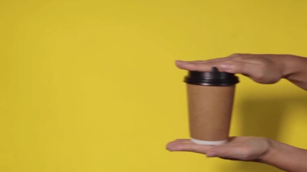 Close-up op een gele achtergrond, een vrouw de hand houdt een papieren beker met koffie in een stand. Koffie of thee te gaan. Mensen geven elkaar een kop koffie en koffie.. - Video
