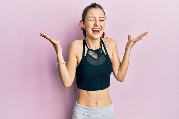 Young brunette woman wearing sportswear celebrating mad and crazy for success with arms raised and closed eyes screaming excited. winner concept  - Fotografie, Obrázek
