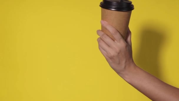 Közelkép sárga háttérrel, egy nő keze egy papírpoharat tart kávéval a lelátón. Kávét vagy teát elvitelre. Az emberek egymás kezét adják át egy csésze kávéért, kávéért.. - Felvétel, videó
