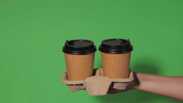 Yeşil arka planda yakın plan, bir kadının eli ayakta kahve olan bir kağıt bardağı tutuyor. Kahve ya da çay. İnsanlar birbirlerine kahve ve kahve dağıtırlar.. - Video, Çekim