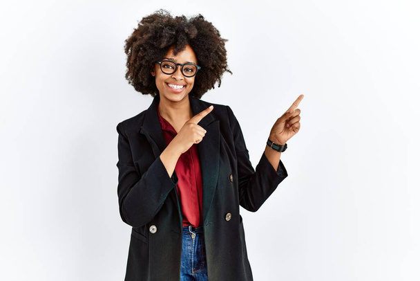 Африканська американка з волоссям афро в діловій куртці і окулярах посміхається і дивиться на камеру з двома руками і пальцями збоку.  - Фото, зображення