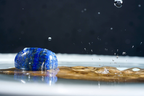 Een blauwe steen in het water met de druppels - Foto, afbeelding