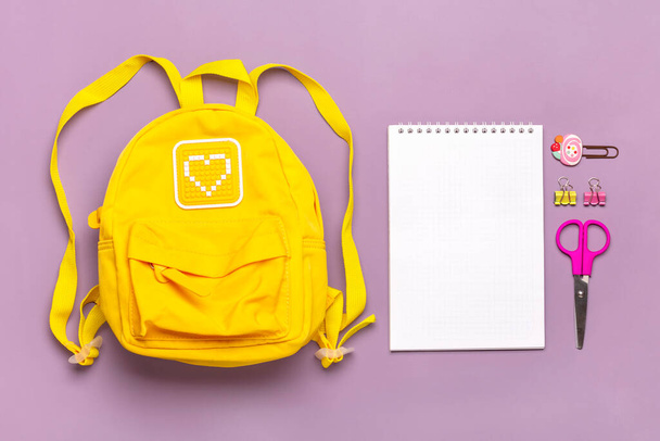 Vissza az iskolába, oktatási koncepció. Sárga hátizsák iskolai felszereléssel - notebook, tollak, klipek, ollók elszigetelt lila háttér Felülnézet Másolás tér Lapos fektetés összetétel Banner - Fotó, kép