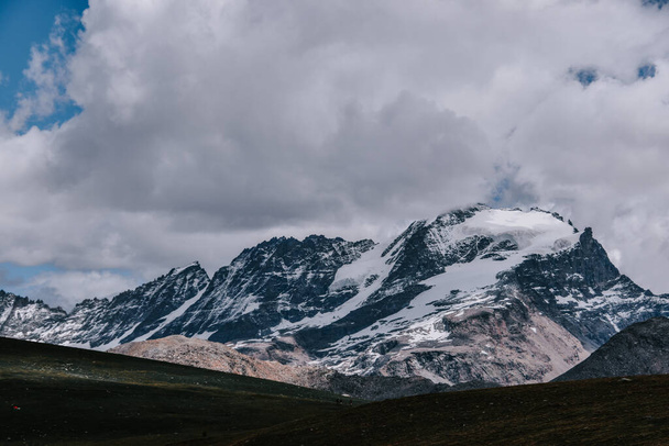 A snow-capped mountain range under a cloudy sky at the Gran Paradiso National Park in the Italian Alps - Fotoğraf, Görsel