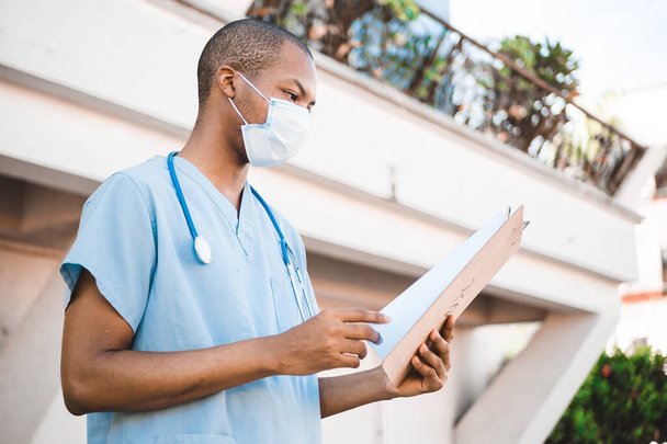 A portrait of an African American young doctor reviewing a check-up chart of a patient - Photo, Image