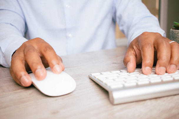 A closeup of a Hispanic businessman's hands as he uses a computer mouse and a keyboard - Фото, зображення