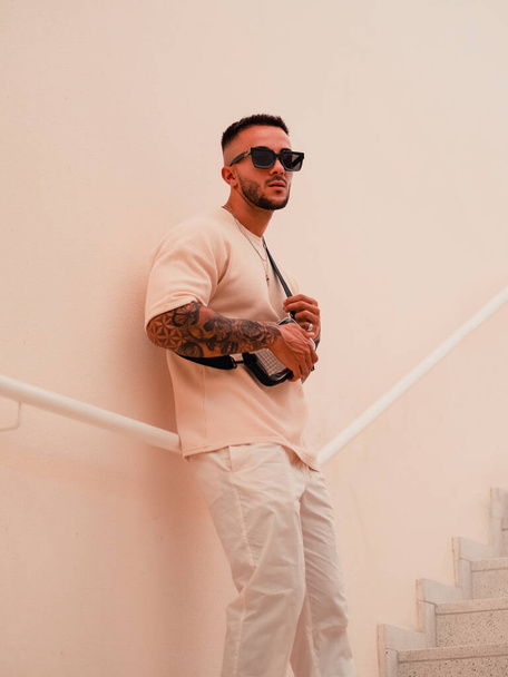 A cool stylish Spanish man with tattoos and sunglasses leaning on handrails on the wall - Foto, imagen