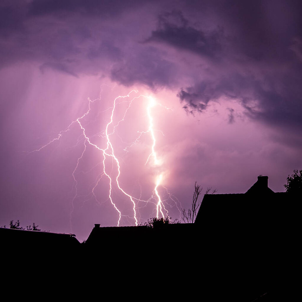 Mehrere Blitzeinschläge färben den Himmel an einem Sommerabend während eines Gewitters violett - Foto, Bild