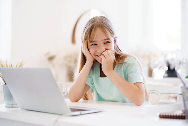Happy little girl pupil using laptop at home - Fotó, kép