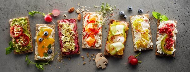 A top view of crispbread toasts with assorted fresh fruits and vegetables arranged in a row - Фото, зображення