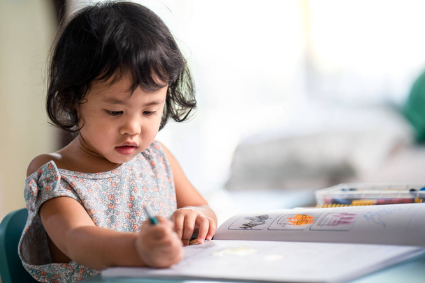 A cute little girl concentrated drawing on the book at the table - Photo, Image