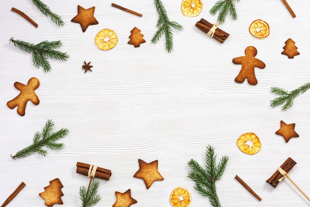 Christmas frame, Christmas gingerbread cookies, pine branches, and cinnamon sticks on white wooden table with copy space, top view, flat lay. New Year figure biscuits. - Foto, imagen