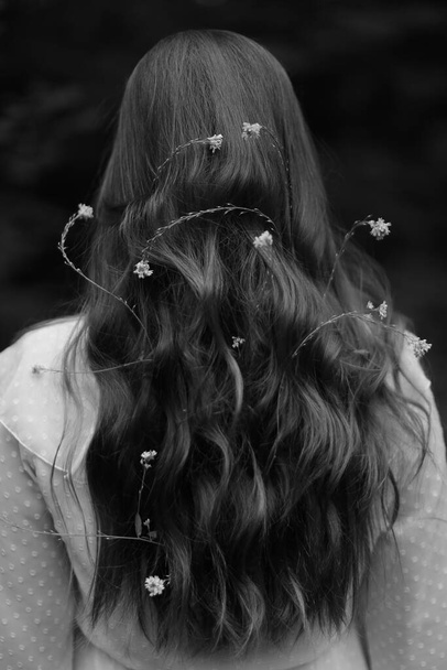 fairy girl with flowers in her hair in a white dress, walking through the forest, black and white frame - Foto, afbeelding