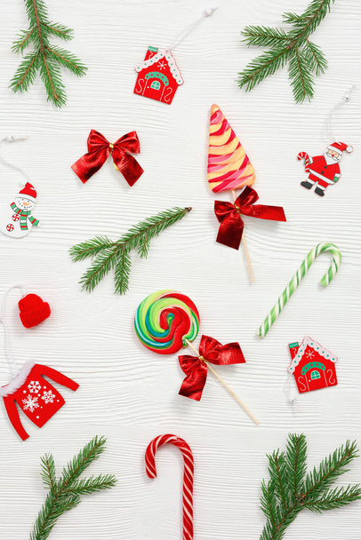 Christmas sweets assorted top view, green fir branches, wooden toys on white background, flat lay. Bright New Year candy and lollipops. - Fotó, kép
