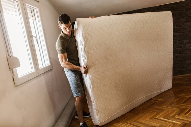 Un hombre lleva un colchón mientras se muda del apartamento - Foto, Imagen