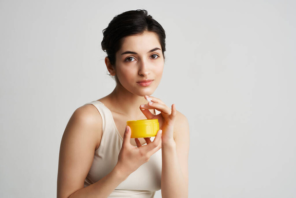 woman with yellow jar of cream cosmetology skin care light background - Фото, зображення