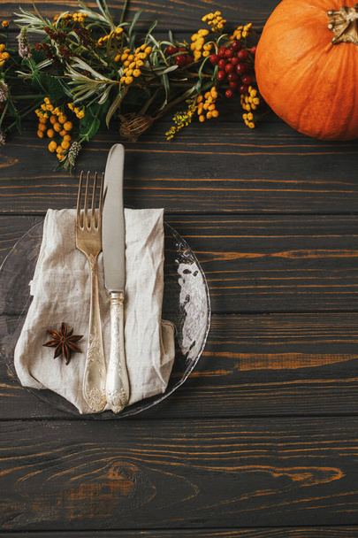 Stylish Thanksgiving dinner table setting. Modern plate with vintage cutlery, linen napkin with anise on wooden table with pumpkins and autumn flowers decoration. Farmhouse rustic autumn wedding - Photo, Image