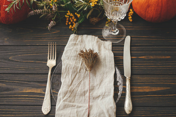 Thanksgiving dinner rustic table setting. Modern plate with vintage cutlery, linen napkin, herb on wooden table with pumpkins and autumn flowers arrangement. Farmhouse autumn wedding catering - Photo, Image