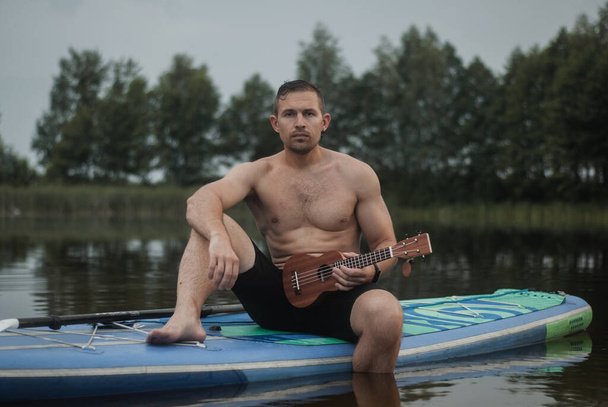 un uomo con un ukulele siede su una tavola da surf - Foto, immagini