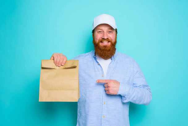 Deliveryman με ευτυχισμένη έκφραση είναι έτοιμη να παραδώσει ένα πακέτο τροφίμων - Φωτογραφία, εικόνα