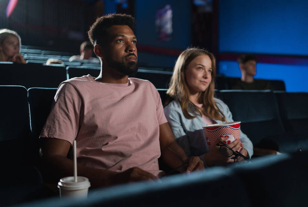 Cheerful young couple with popcorn in the cinema, watching film. - Foto, imagen