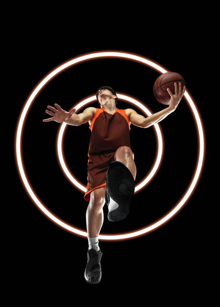 Abstract desing, concept of sport, action, motion in sport. Young sportive man playing basketball isolated on black background with neon luminescent geometric figures - Foto, Imagem