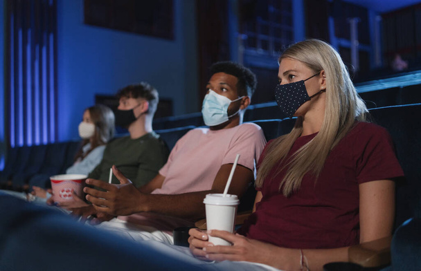 Young people watching film in the cinema, coronavirus concept. - Photo, Image