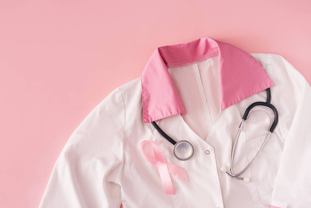 Pink ribbon and stethoscope on white coat on pink background. - Фото, зображення