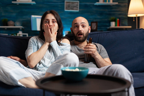 Confused shocked couple watching TV movie at night and eating popcorn, - Photo, Image