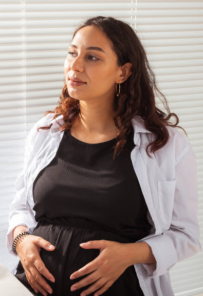 Portrait of hispanic pregnant woman at home. Pregnancy, health and maternity leave concept. - Photo, image