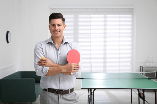 Businessman with tennis racket and ball near ping pong table in office. Space for text - Zdjęcie, obraz