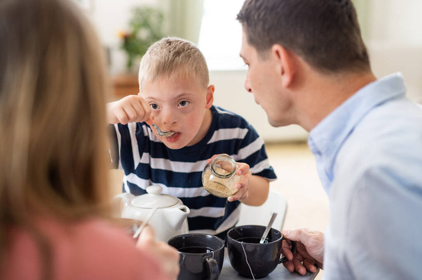Famiglia felice con la sindrome di Down figlio a tavola, facendo colazione. - Foto, immagini