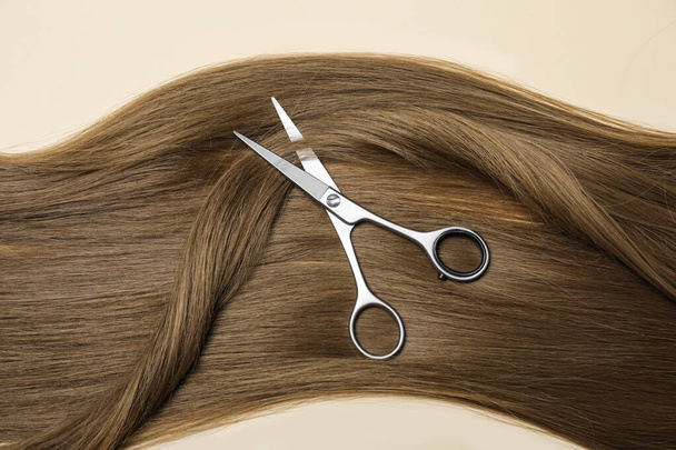 Professional hairdresser scissors with dark blonde hair on beige background, top view. Haircut tool - Photo, Image