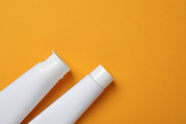 Blank tubes of toothpaste on orange background, flat lay. Space for text - Фото, изображение