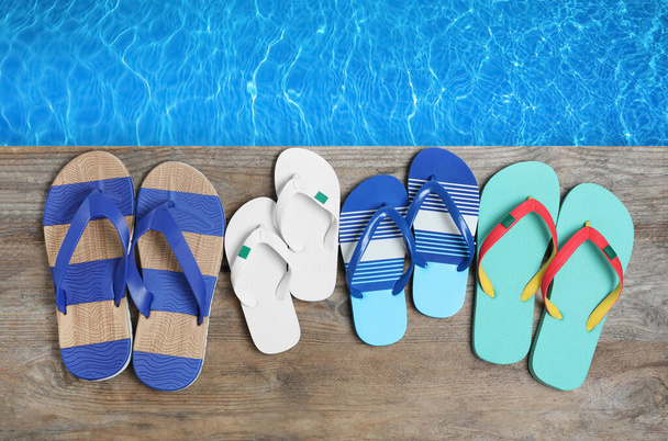 Pairs of flip flops on wooden deck near swimming pool, flat lay  - Photo, Image