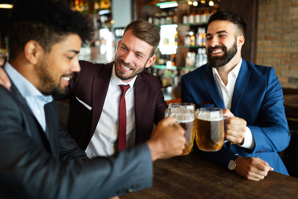 Meeting with the best friends. Happy young men talking and drinking beer while sitting in bar together - 写真・画像