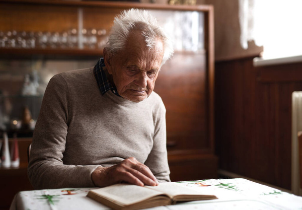 Portrait of elderly man sitting at the table indoors at home, resting. - Foto, Bild