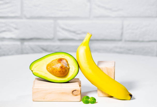 Creative avocado, banana and micro green balance wooden stands and podiums., white background, Equilibrium healthy food. Balanced nutrition concept - Foto, afbeelding
