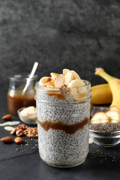 Delicious chia pudding with banana, walnuts and caramel sauce on black table - Photo, image