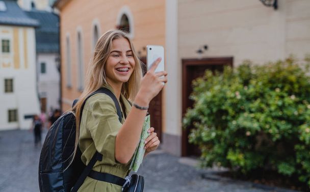 Young woman tourist outdoors on trip in town, taking selfie with smartphone. - Fotoğraf, Görsel