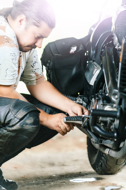 Mutiger junger Mann repariert sein leistungsstarkes Motorrad. - Foto, Bild