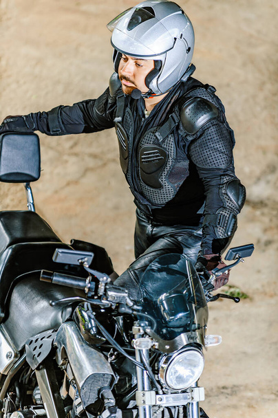 Motociclista en un casco y el engranaje cuesta cerca de una motocicleta potente grande. - Foto, imagen
