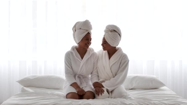 Home Spa. Δύο χαμογελαστές Αφρο-Αμερικανίδες Αδελφές που φοράνε μπουρνούζια στο κρεβάτι - Πλάνα, βίντεο