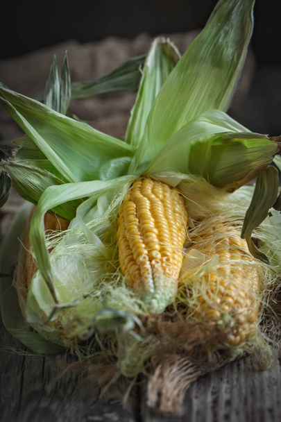 Fresh juicy corn with leaves on a wooden table. Autumn background. Selective focus. - 写真・画像