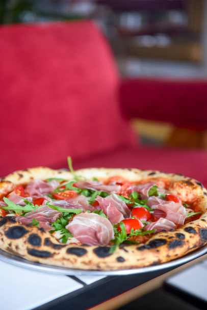 Pizza prosciutto with ham, tomato and mushrooms served on a round tray on a table inside a restaurant. Traditional Italian pizza recipe. - Photo, Image